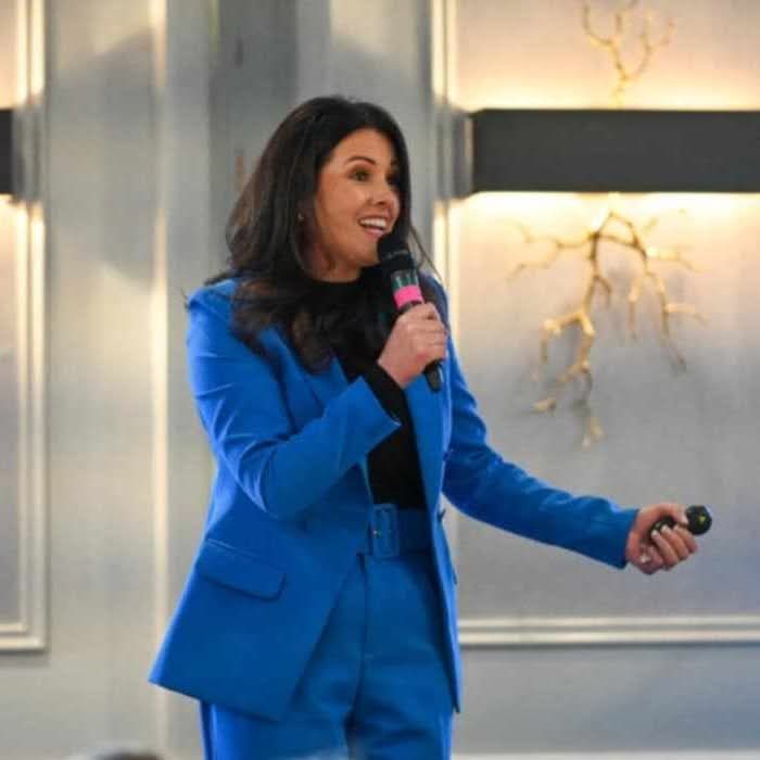 Louise McDonnell speaking on stage at a marketing event in a bright blue suit
